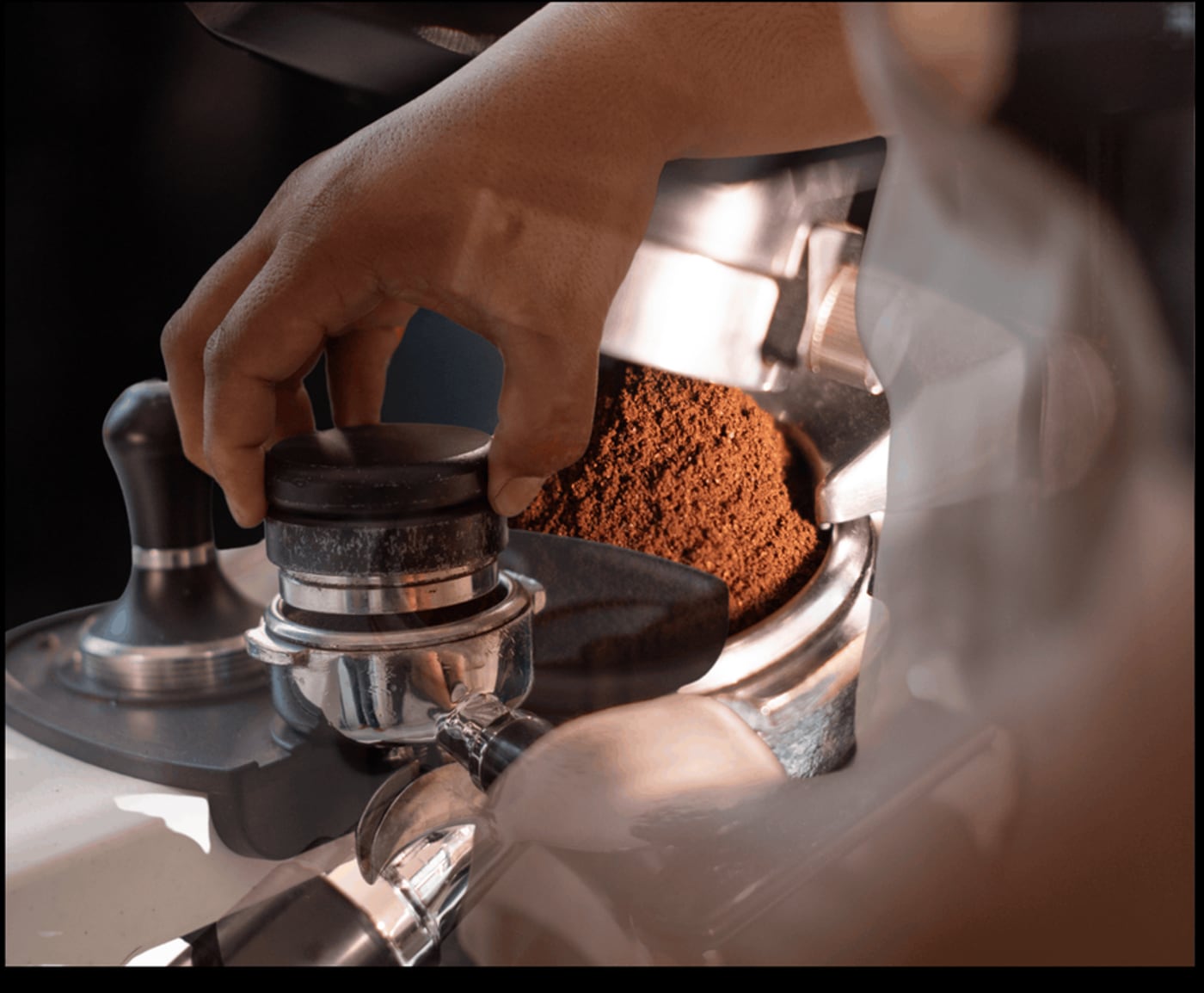 A barista tamping a fresh dose of ground coffee into a portafilter