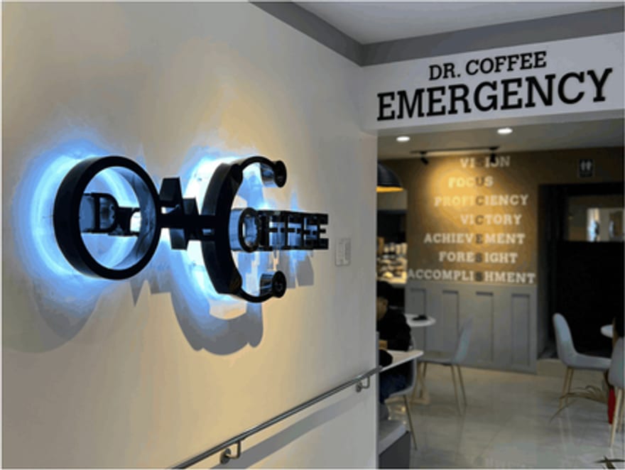 The illuminated Dr. Coffee logo glowing on the wall by the stairs